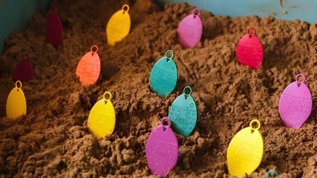 Peixes de plástico coloridos fincados em um monte de areia marrom.