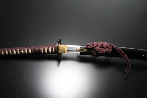 A Japanese katana againt a black backdrop with purple decorative pieces slightly unsheathed 