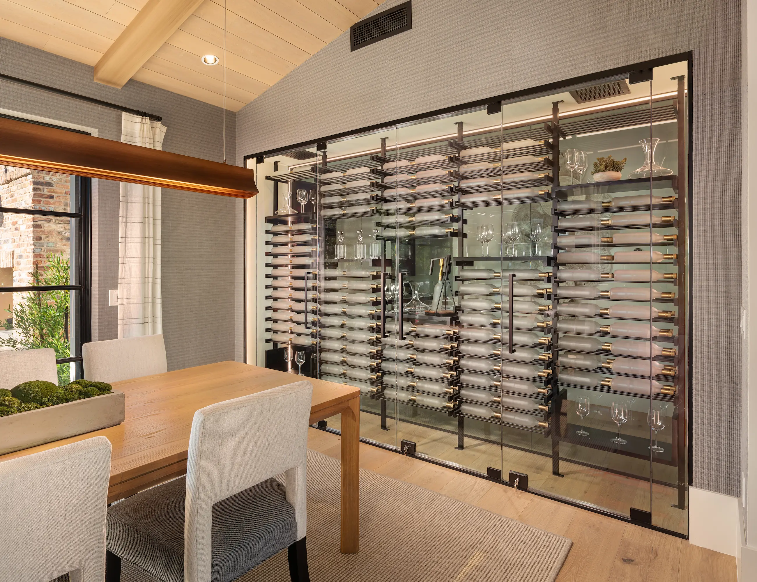 Modern glass-enclosed wine wall with black anodized metal racking and walnut shelving in a luxury dining room — custom wine cellar design by Innovative Wine Cellar Designs.