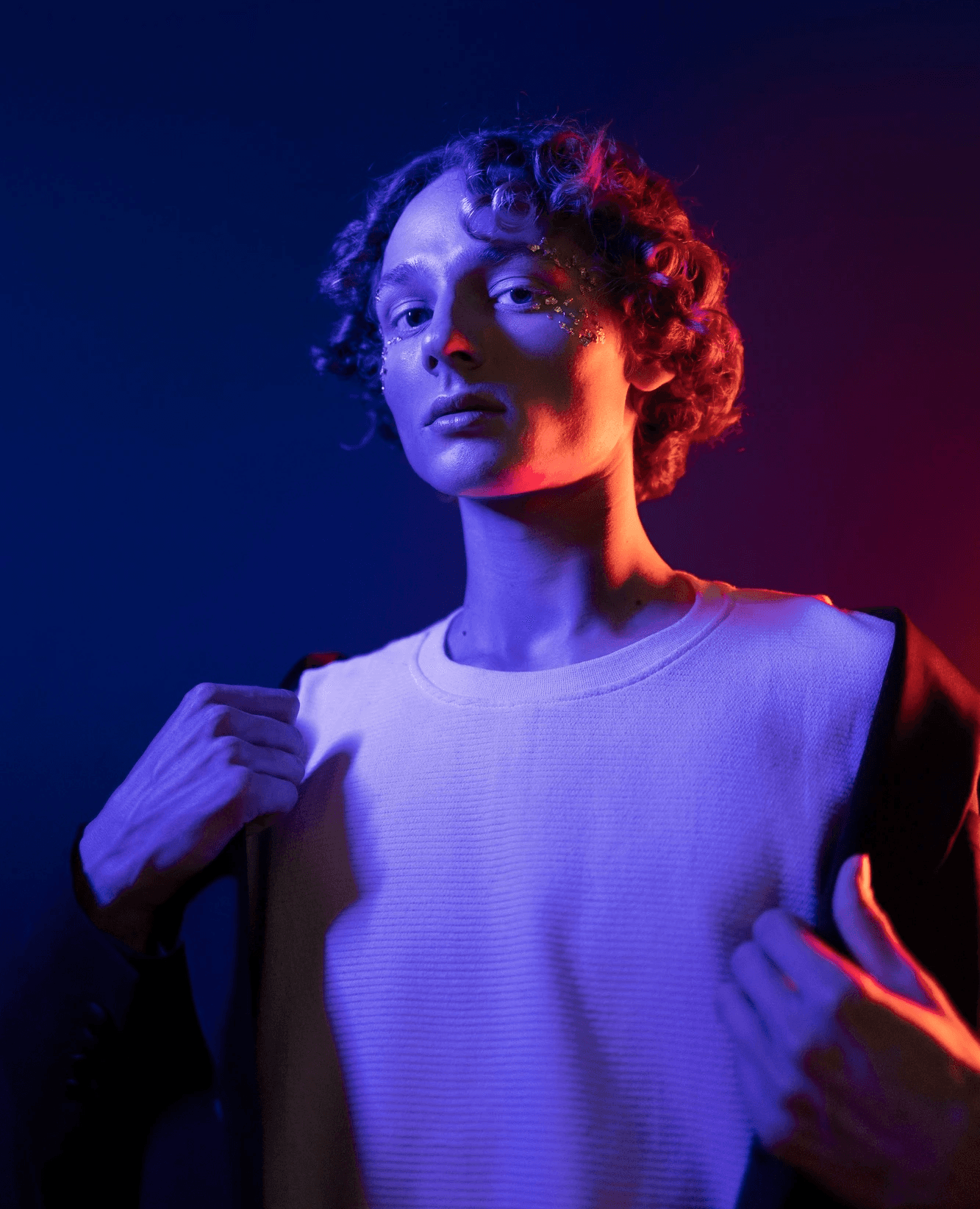 Artistic portrait of a man with glitter on his face, captured with dual-tone purple and red rim lighting for a cinematic, futuristic look.