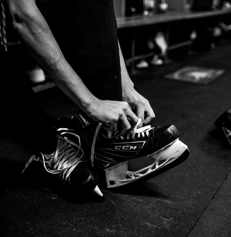Close-up of player lacing CCM hockey skates in locker room, showcasing preparation rituals that contribute to elite performance.