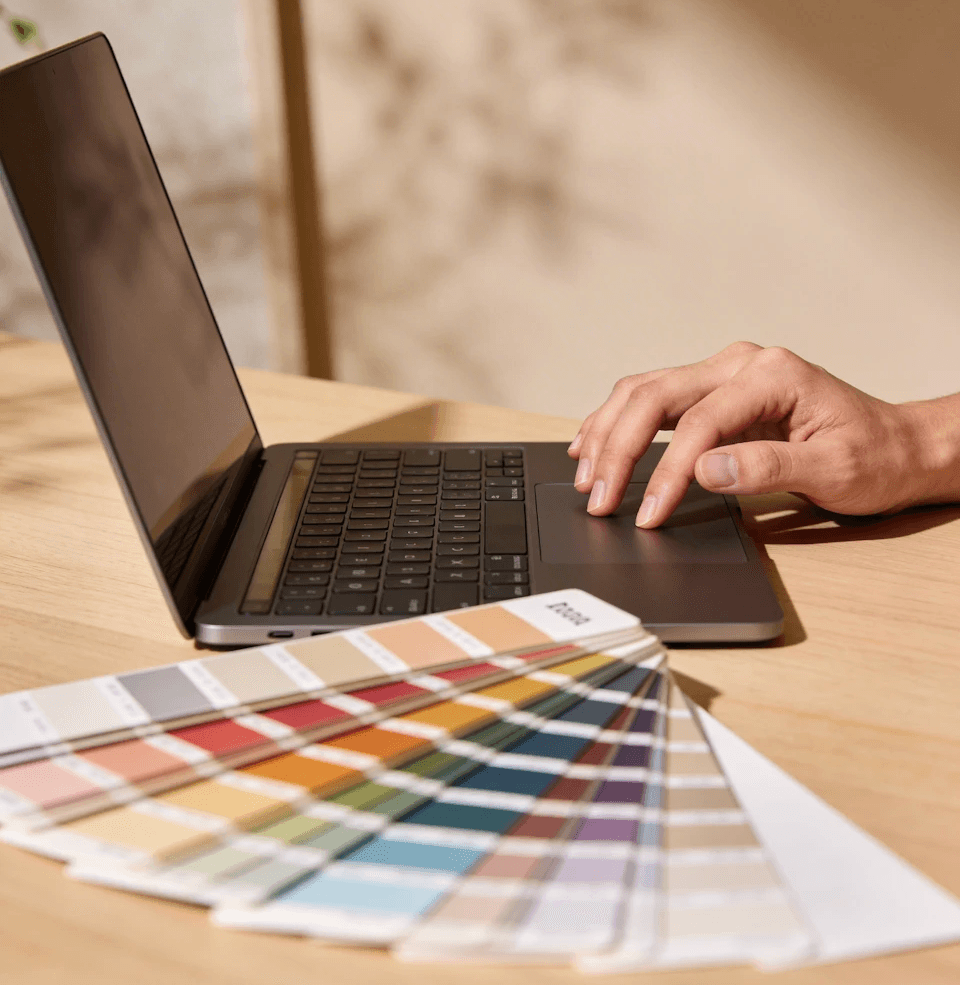 Hand using laptop trackpad beside open color swatch book