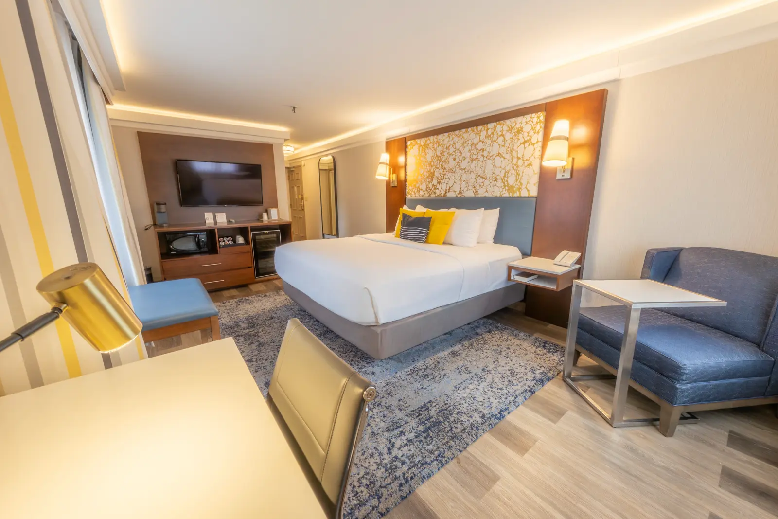 Modern hotel room with a bed, desk, and sofa.