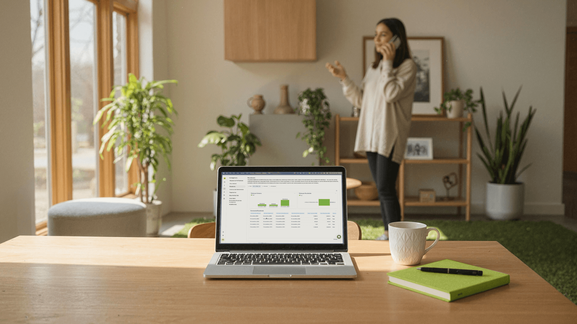 Laptop exibindo um painel financeiro da Tivita com gráficos e indicadores de recebimentos, sobre uma mesa com caderno e xícara, enquanto uma pessoa ao fundo fala ao telefone. A imagem representa o uso de dados para gestão financeira em clínicas.