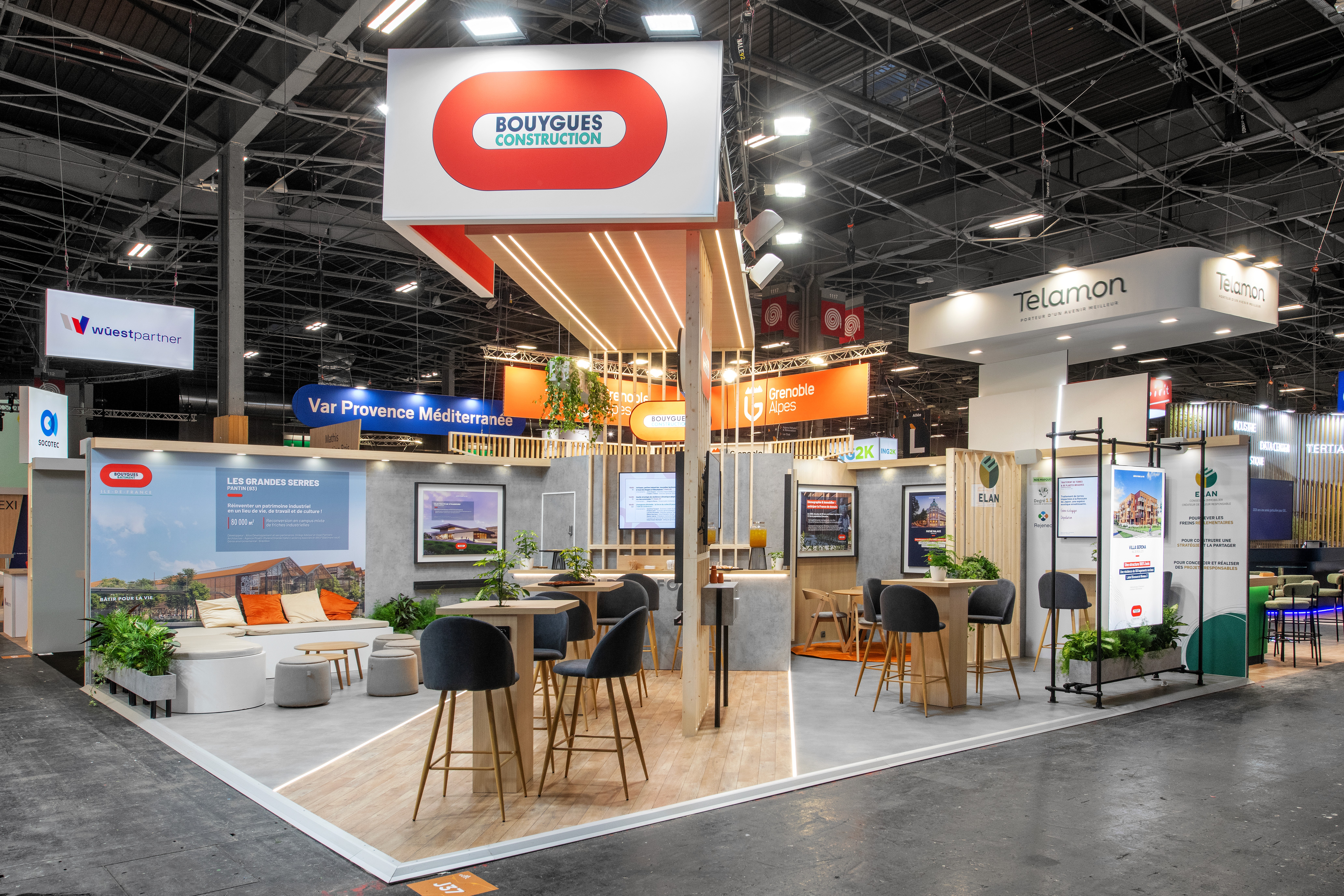 Stand Groupe Bouygues SIMI 2025 Paris réalisé par Expace – vue trois quarts du stand avec structure modulaire orange et blanche, espaces d'échange et mobilier contemporain