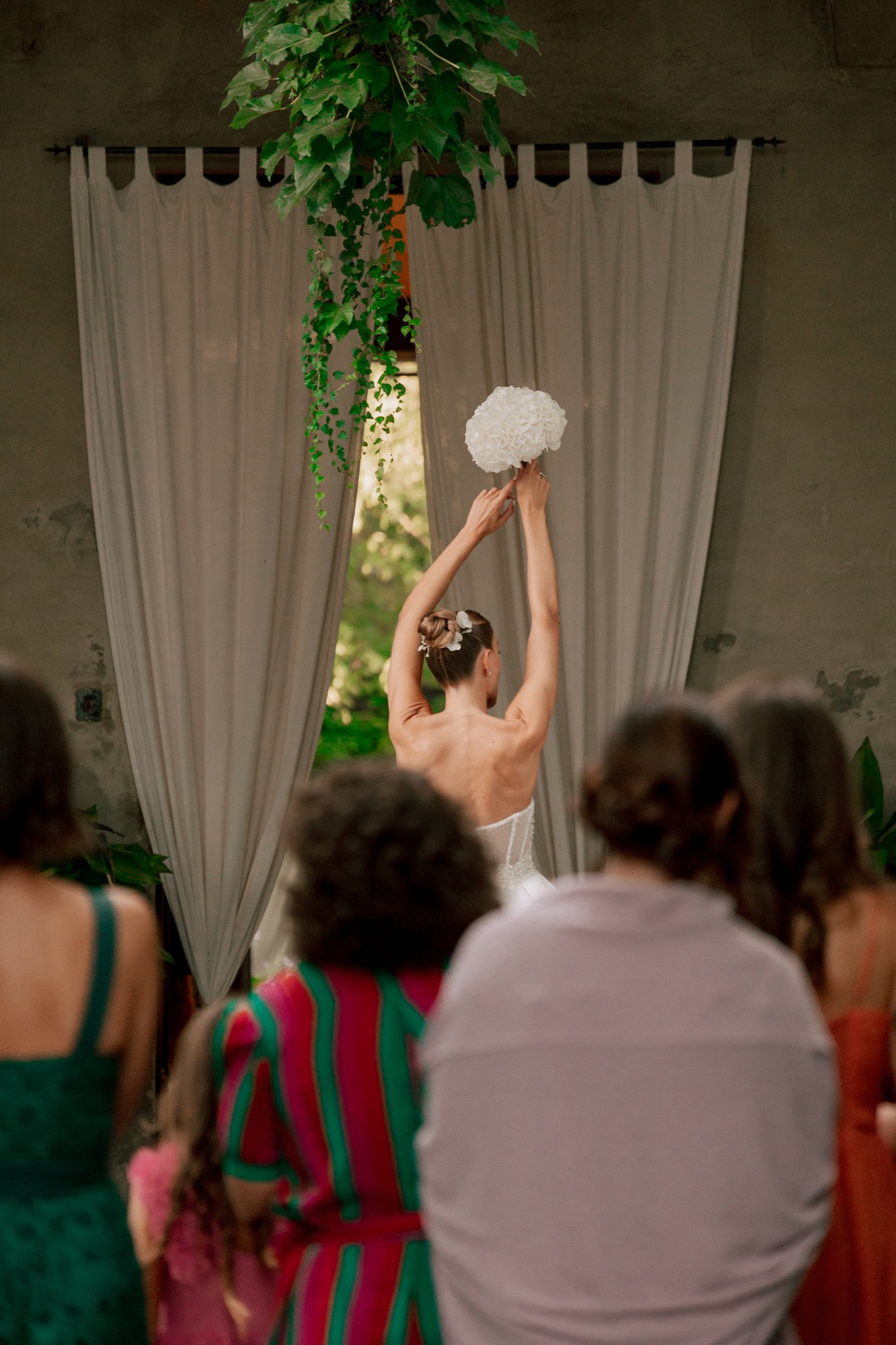 Sposa alza il bouquet sotto l'installazione floreale, ospiti guardano il momento al ricevimento di Villa Ferrari