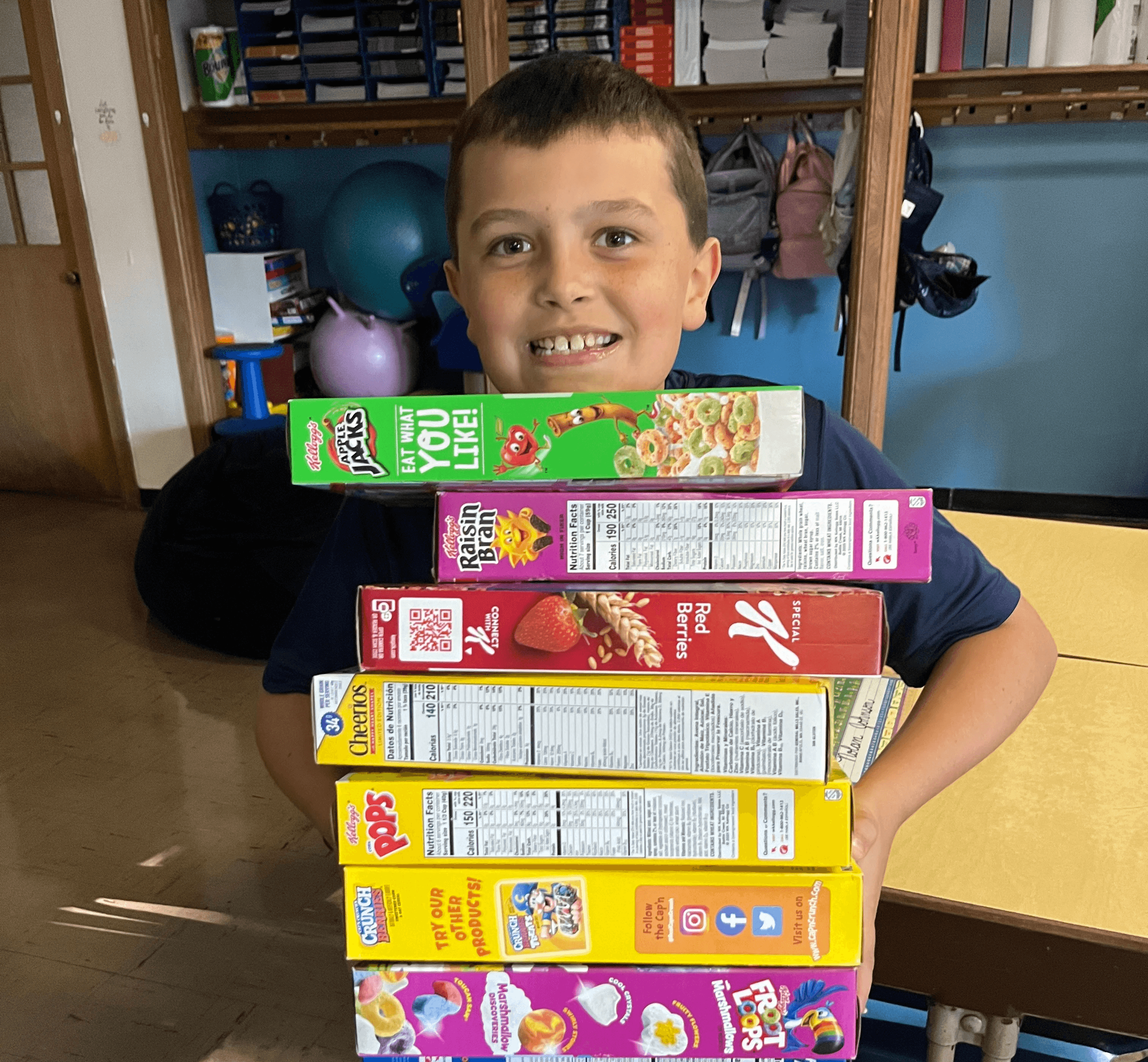 A student holding a tall stack of cereal boxes collected for a food drive