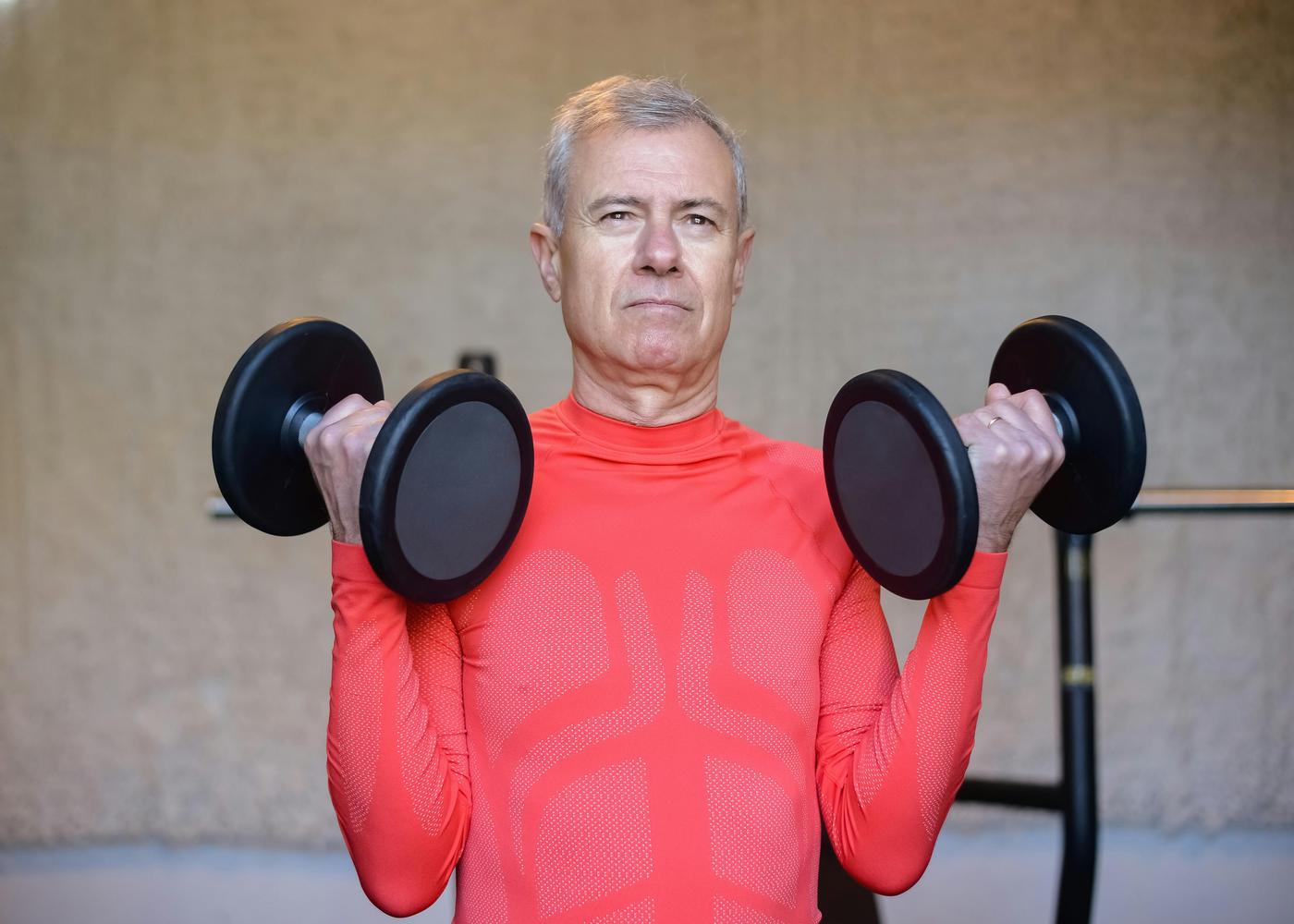 Elderly man lifting two heavy dumbbells