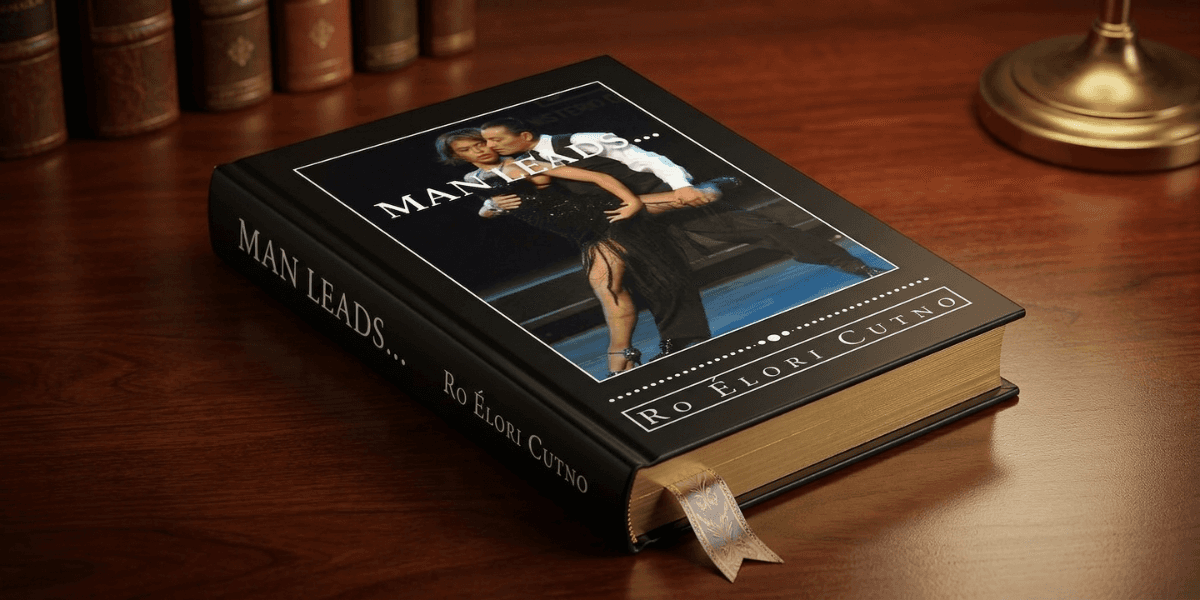 A hardcover book titled "Man Leads" by Ro Èlori Cutno rests on a wooden table. The cover features a couple dancing passionately. A gold ribbon is placed inside.