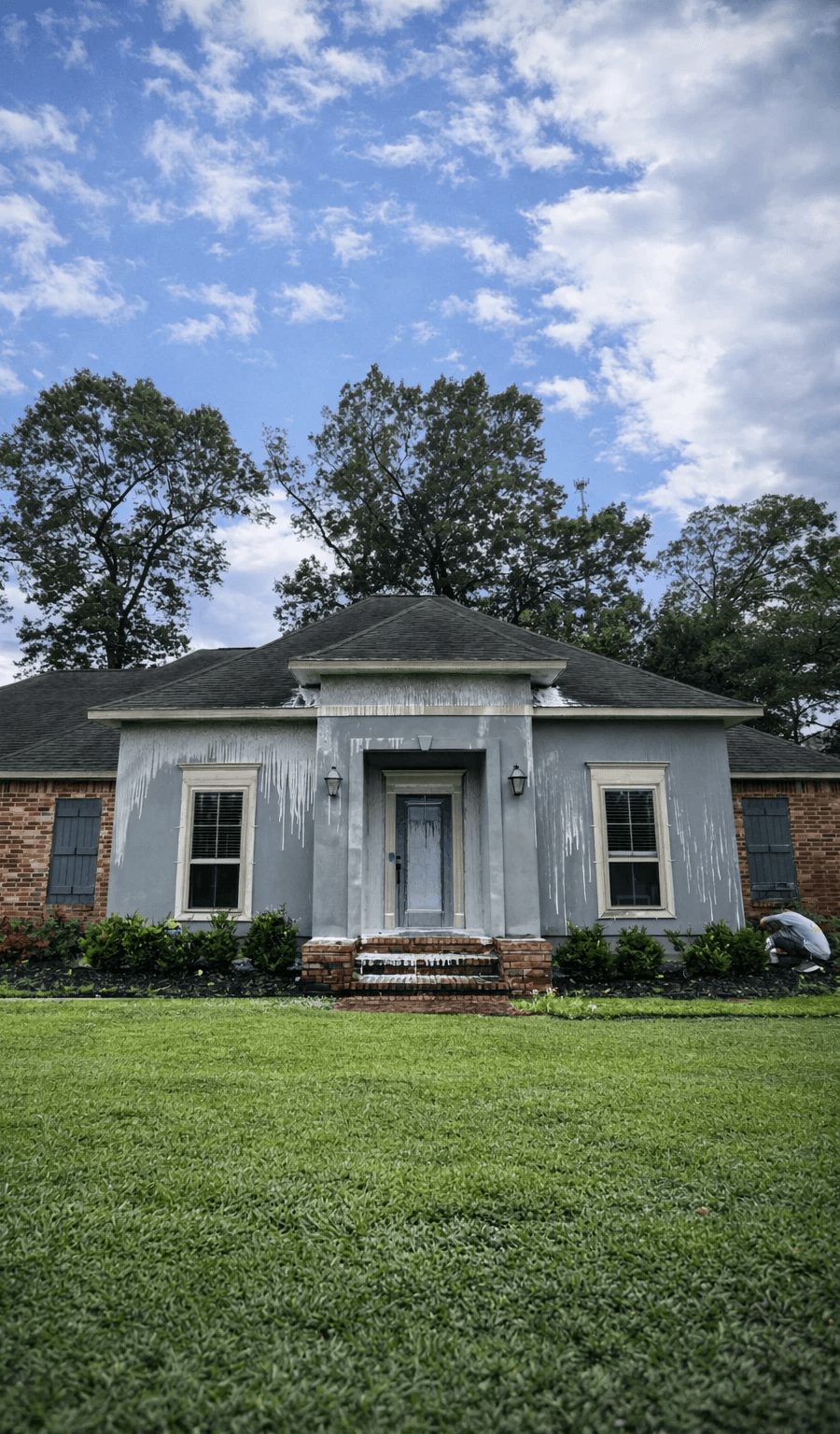 A modern, luxury beachfront villa with large glass windows and balconies overlooks a rocky shoreline, surrounded by palm trees at sunset.