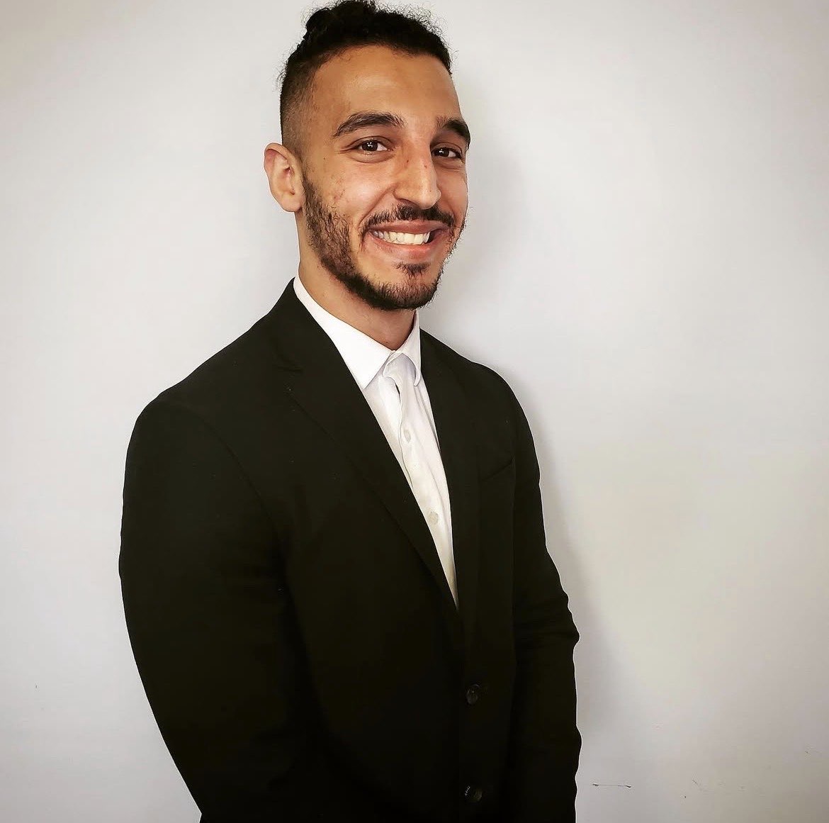 A woman with short curly hair wearing a black t-shirt looks into the camera.