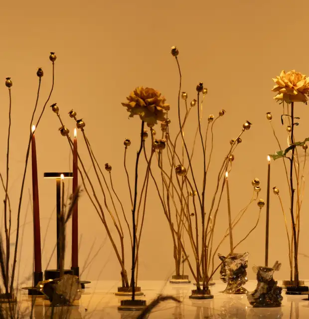 Composición artística con flores secas doradas y velas encendidas sobre superficie blanca, creando una atmósfera cálida y minimalista.