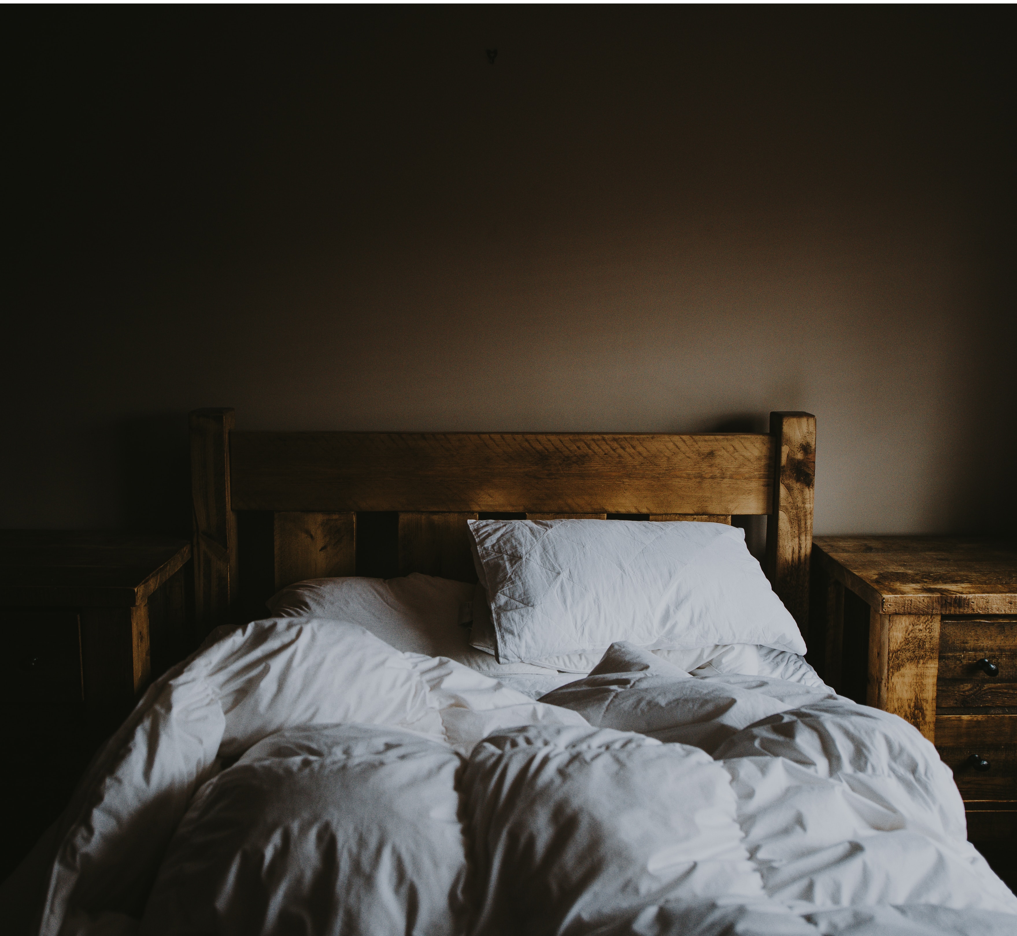 bed in a low lit room with white sheets