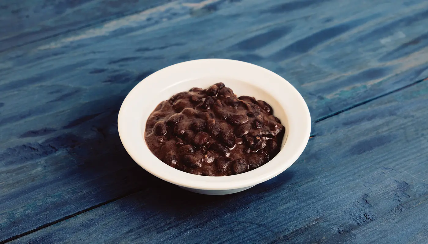 Side of Black Beans in a white bowl on blue wooden boards.