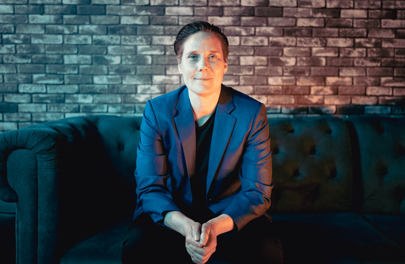 Headshot of Tuulia Virhiä, CEO of SwanIT, sitting on a dark couch against a brick wall