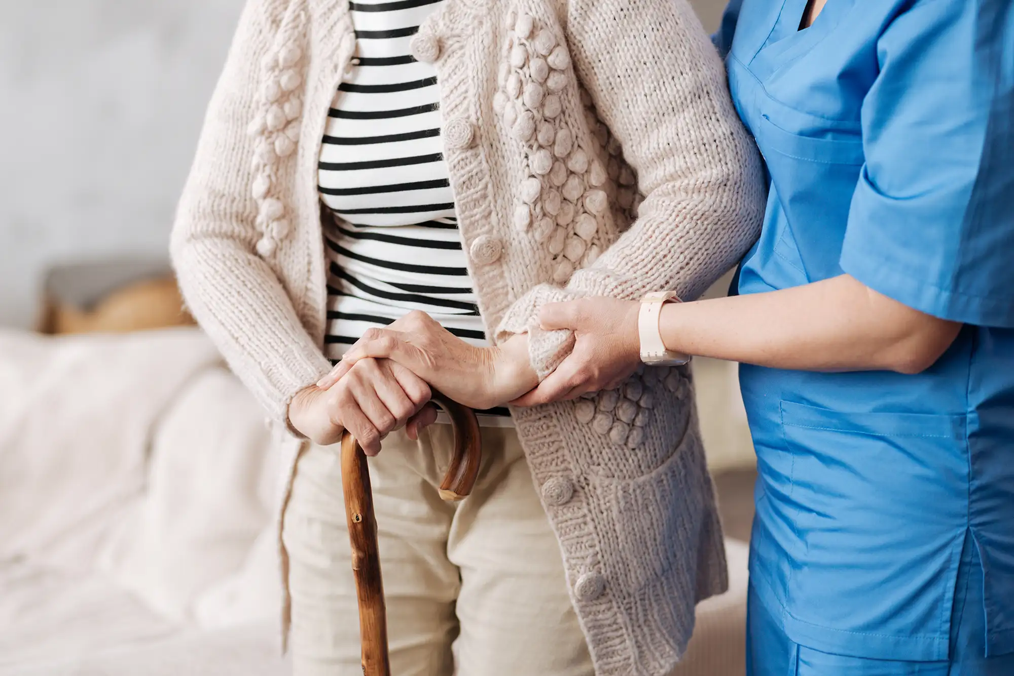 Caregiver assisting an elderly woman with a cane indoors