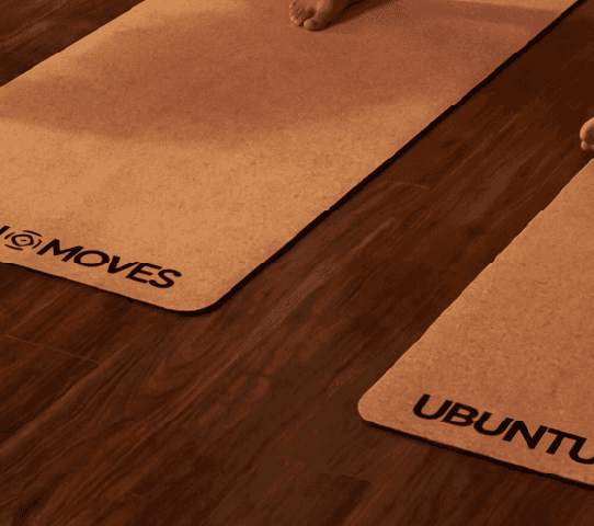 Diverse group practices yoga on cork yoga mats in a warm studio: warrior, tree, and seated poses.