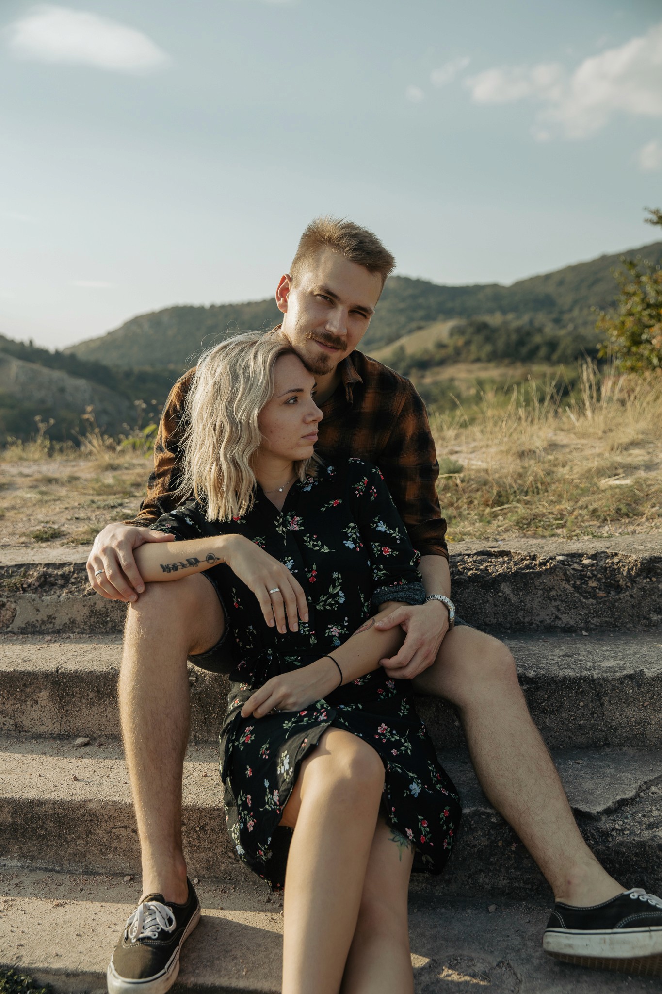 Fiatal pár ül a lépcsőn, a nő virágos ruhát visel, a férfi karolja őt.