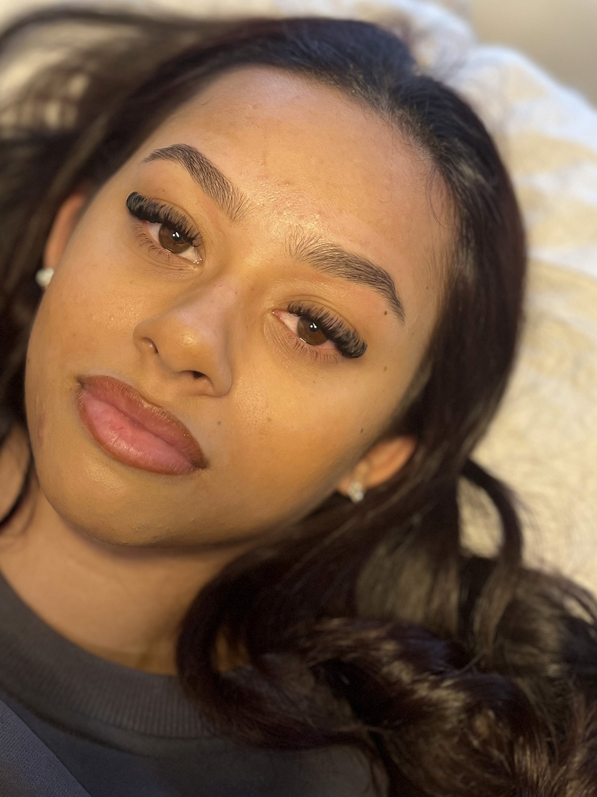 A woman with long eyelashes and smooth skin gazes upward. Her expression is calm and relaxed, with soft lighting enhancing her features.