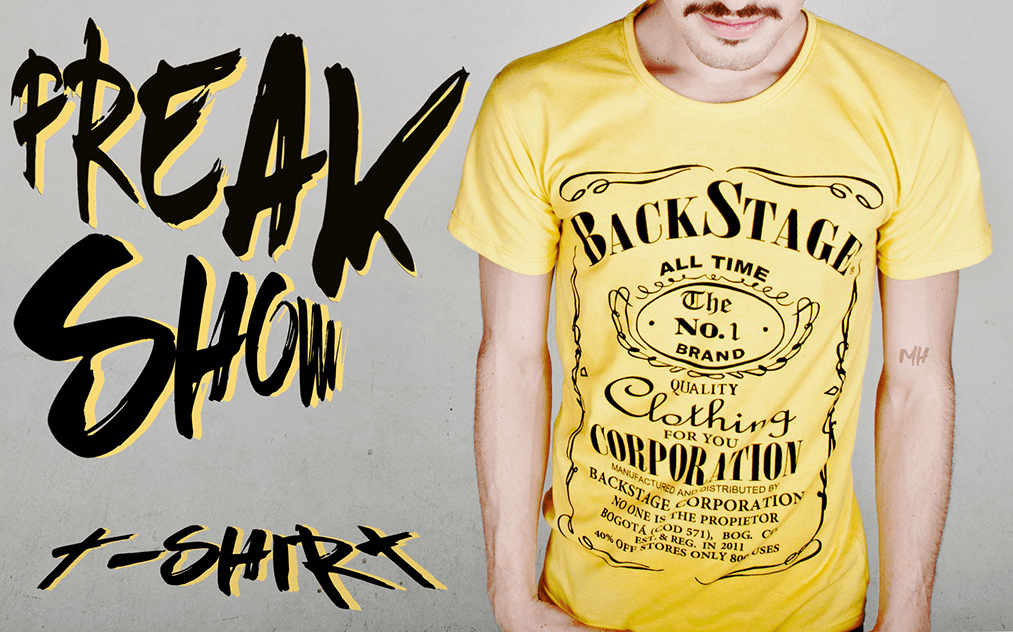 Frontal shot of a man wearing a yellow t-shirt with a vintage "BACKSTAGE" liquor-label style graphic. Large black "FREAK SHOW" text is overlaid on the left.