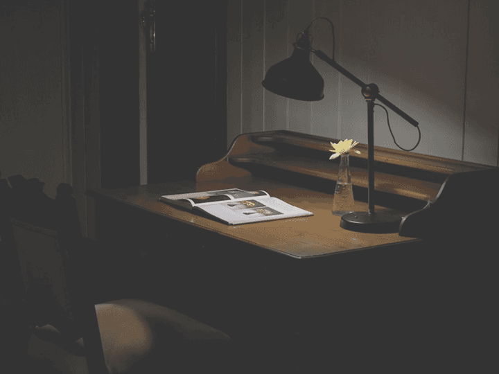 A minimalist dark wooden desk with a single lamp illuminating a blank page, illustrating 'The Anatomy of a Thriller'.