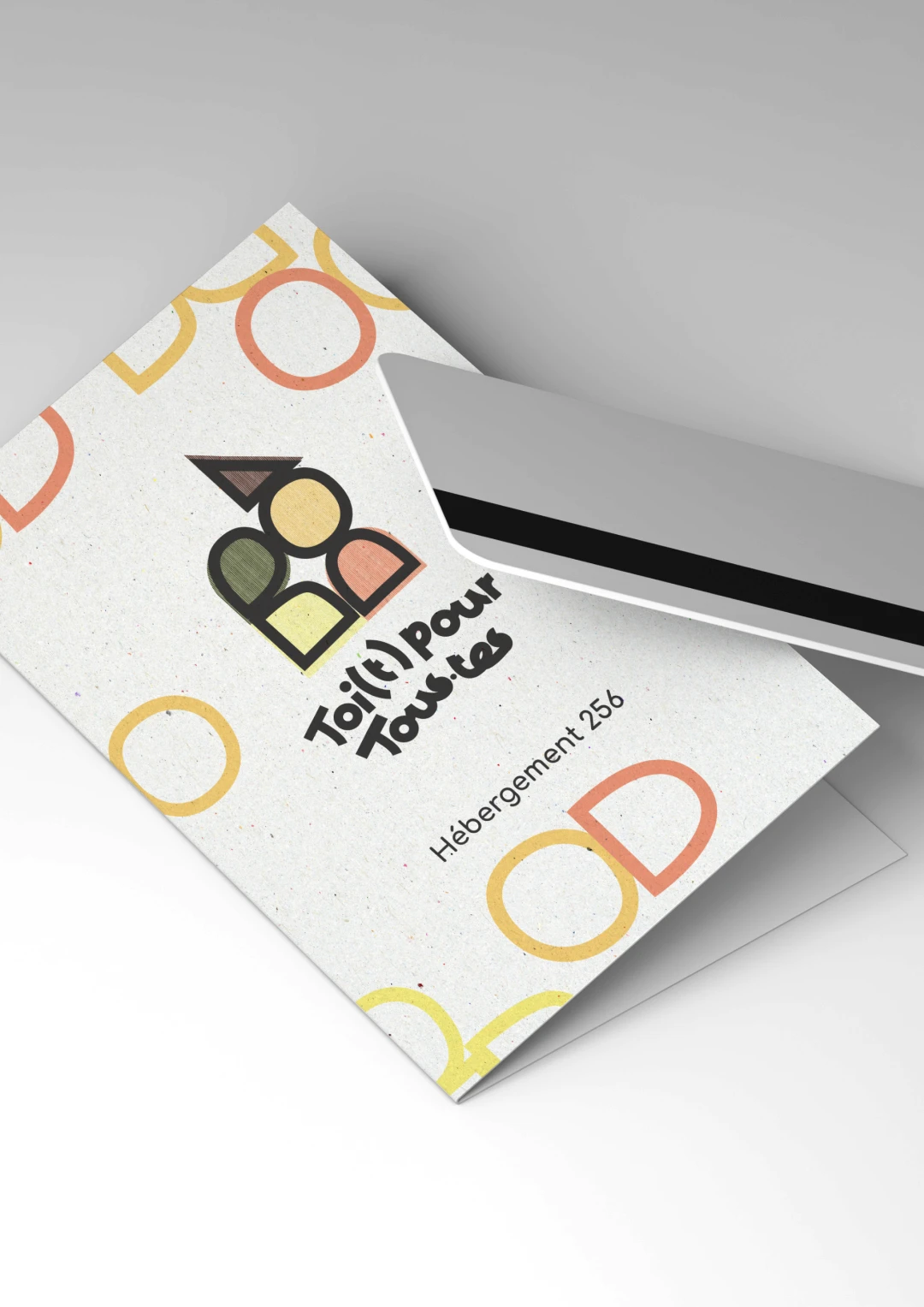 Mockup carte d'hébergement Toi(t) Pour Tous·tes sur papier recyclé texturé — logo couleur et motif géométrique Bauhaus, déclinaison print écoconçue, design graphique Tartelette Concept Toulouse