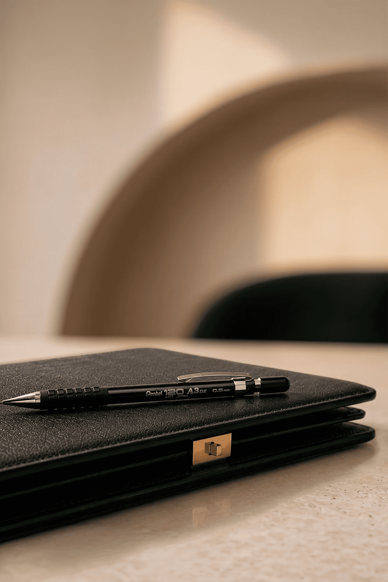 A sleek green leather notebook with a gold clasp and a black pen resting on a marble surface in a warmly lit, elegant room, labeled "01 Discover."