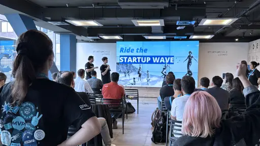 Audience listens to a presentation in the event "Ride the Startup Wave" in a modern conference room.