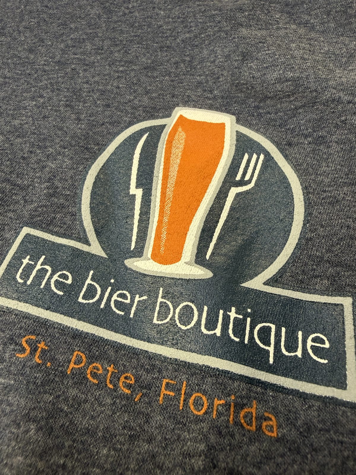 Cream and orange beer-glass artwork and lettering printed on gray fabric, shown close up.