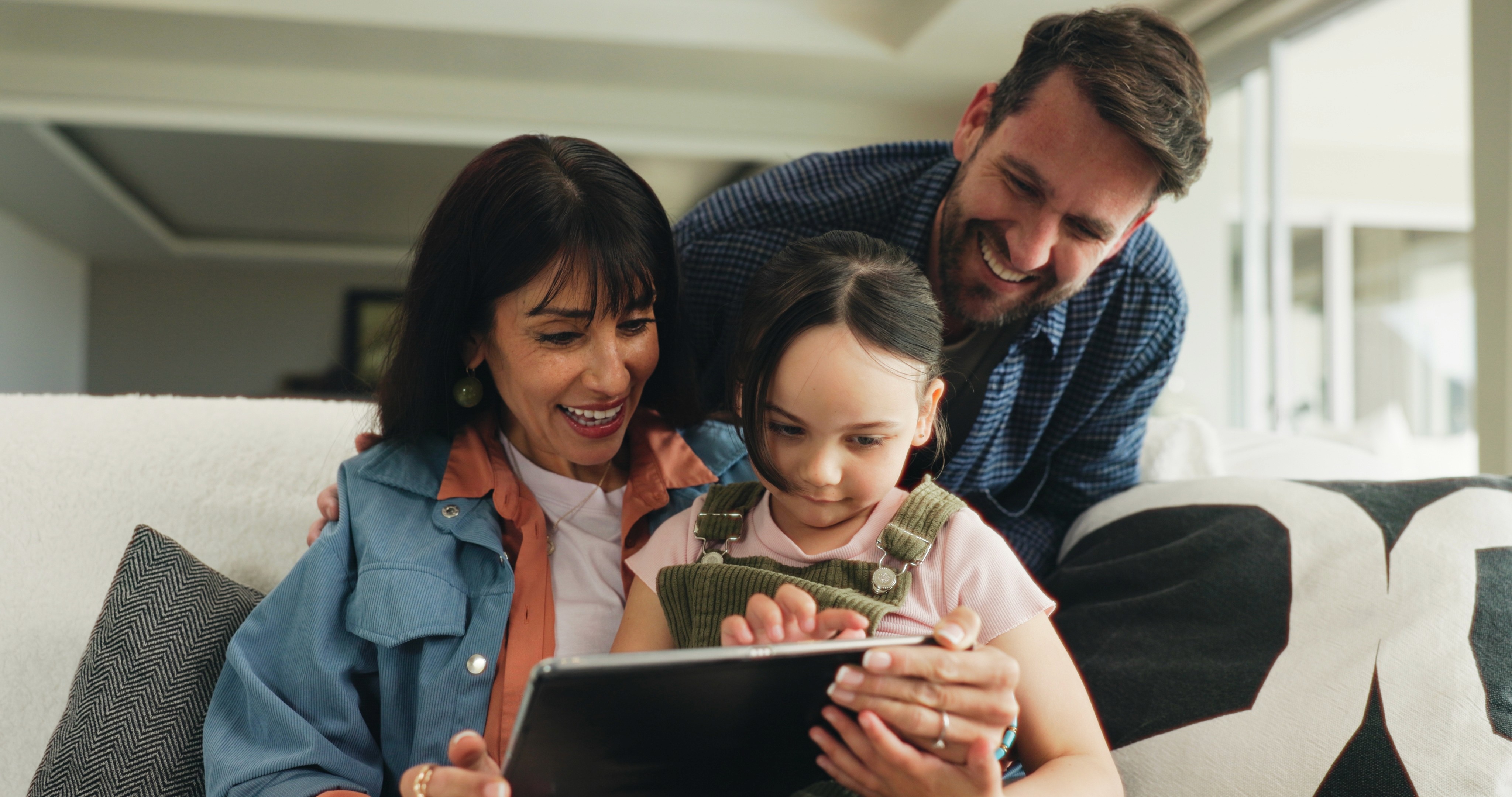 Man with glasses and tied-back hair writing on a tablet while seated at a desk in a softly lit room.