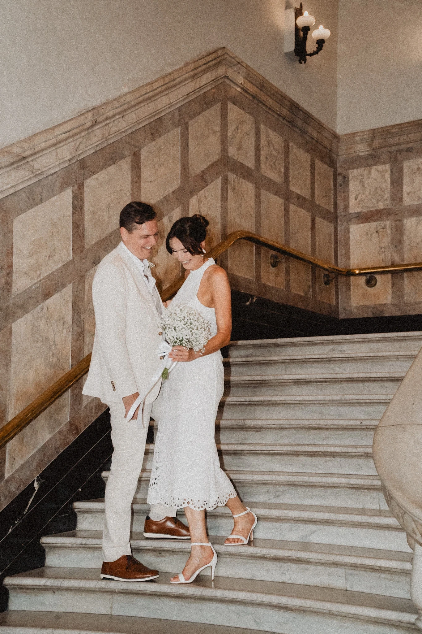 Bride and groom leaning together on a stone staircase inside an ornate building.