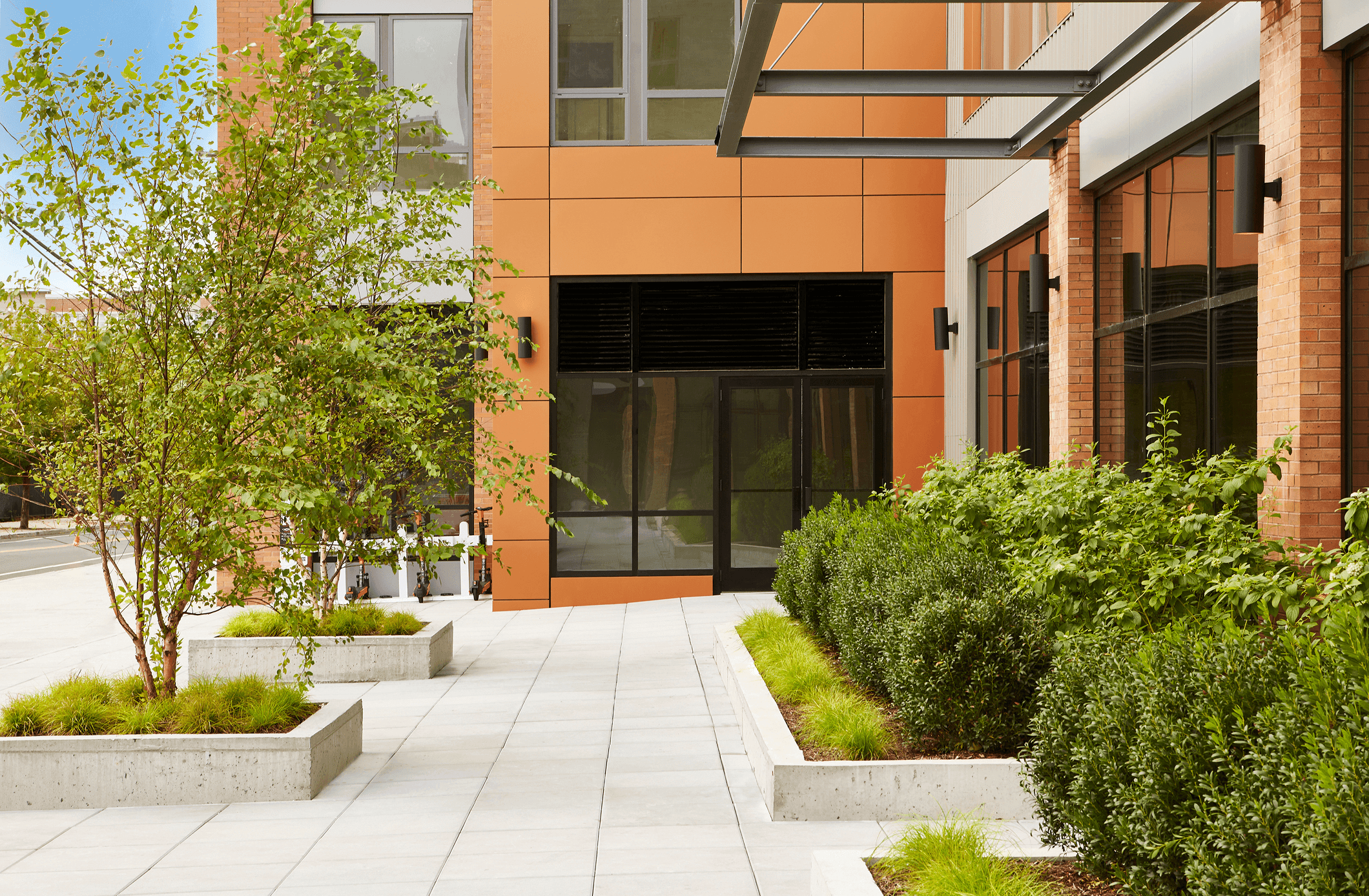A modern building entrance with large glass doors, surrounded by well-maintained greenery and landscaped paths.