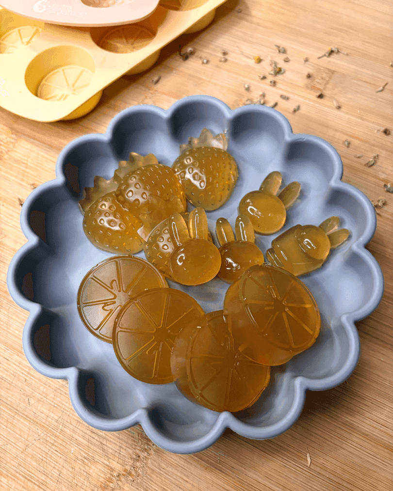 Homemade chamomile gummies in fruit and bunny shapes served in a scalloped silicone bowl on a wooden surface.