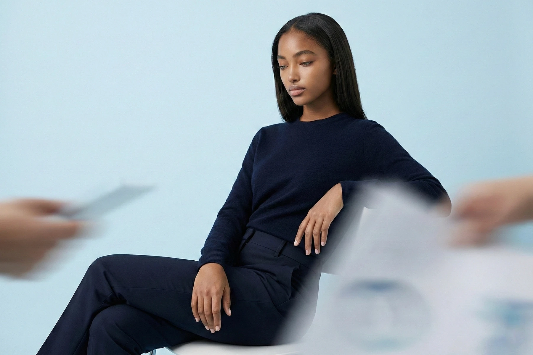 Eine entspannte Unternehmerin sitzt ruhig da, während verschwommene Hände im Vordergrund Papierkram erledigen – ein Symbol für die Befreiung von Routineaufgaben durch unsere KI Automatisierung Agentur Köln.