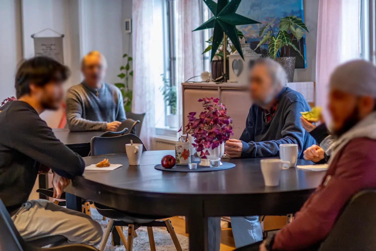 Människor i samtal runt ett bord under en gemensam fikastund.