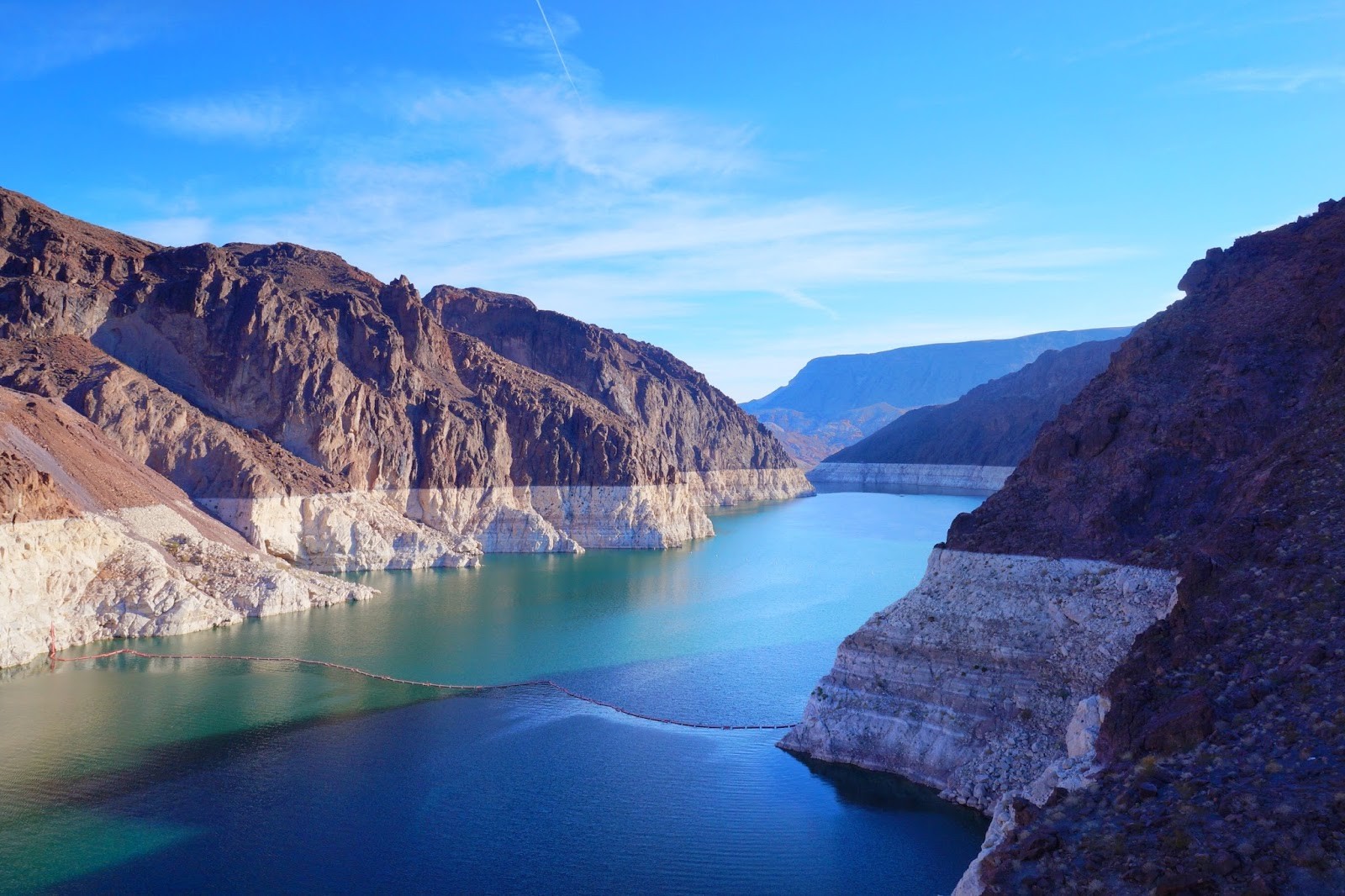 2 red helicopters are flying over the impressive Hoover Dam and Lake Mead