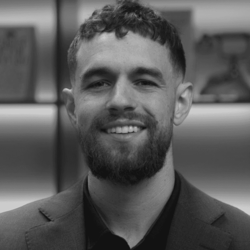 Smiling man with a beard and short curly hair, wearing a suit jacket and looking at the camera.