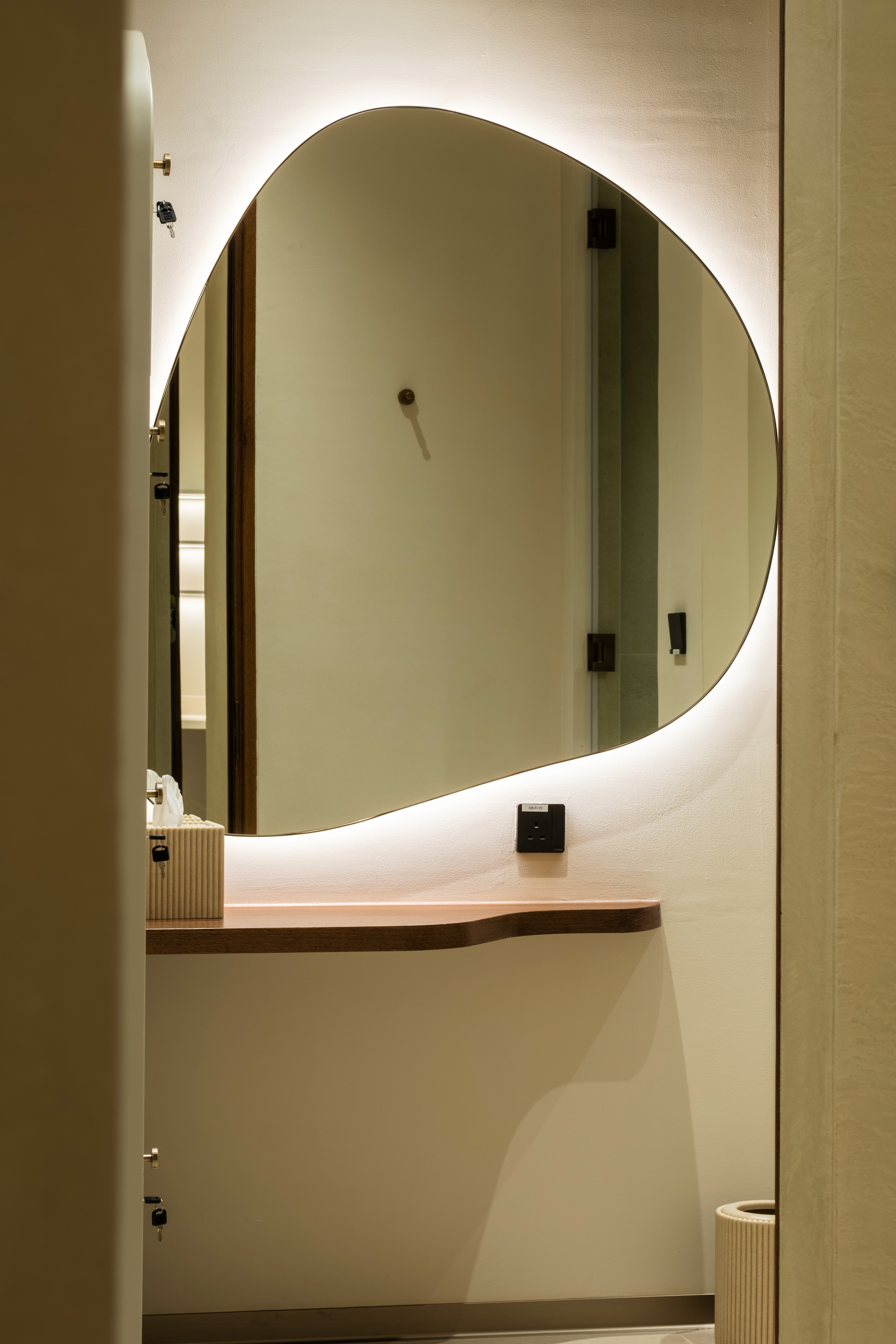 Luxury gym amenity shelf with backlit dark shelving holding matte black kettlebells, medicine balls, and folded white towels, alongside a marble counter with glass water carafes