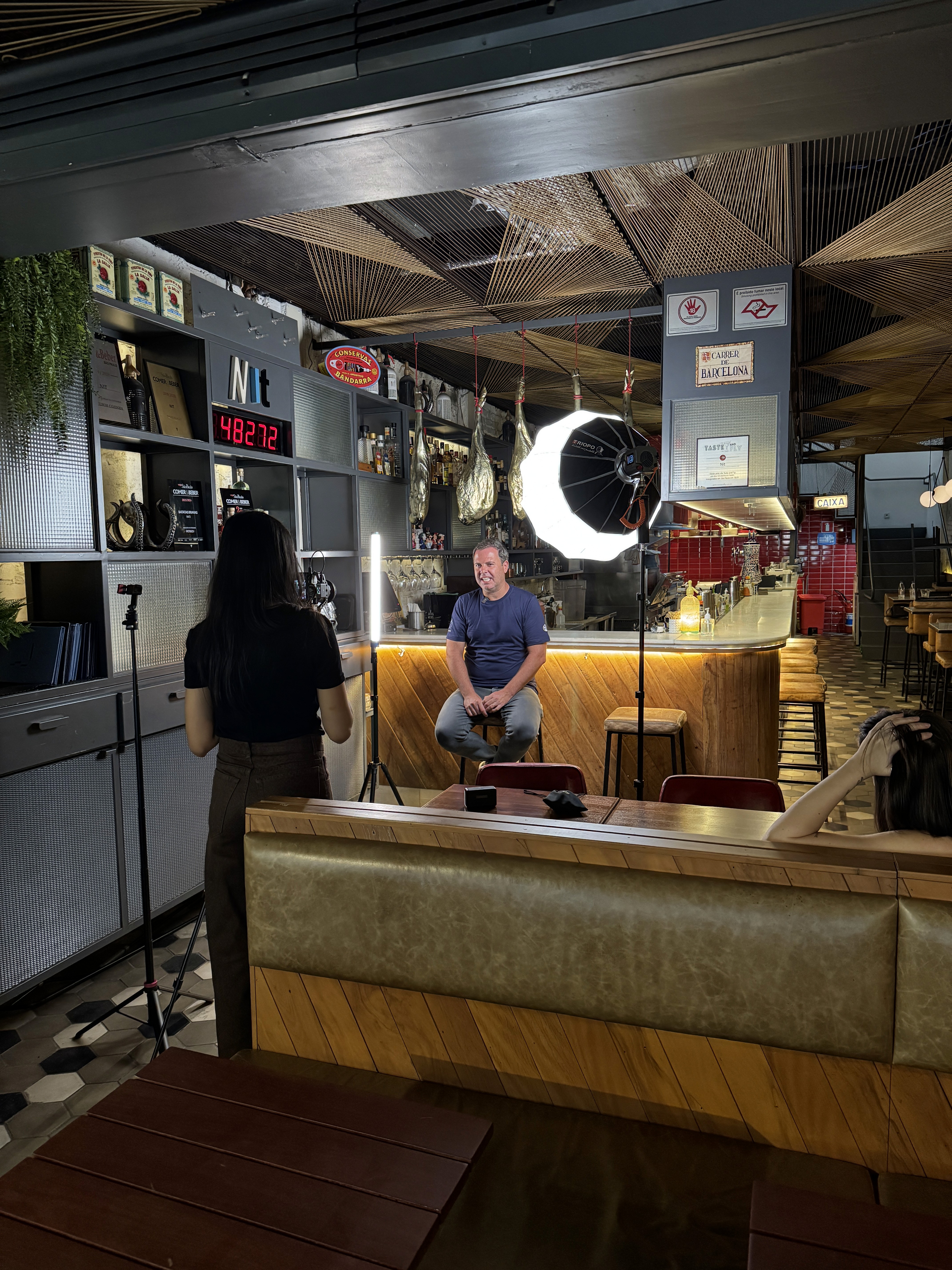 A smiling young man with crossed arms, wearing a plaid shirt and white t-shirt, poses against a dark background.