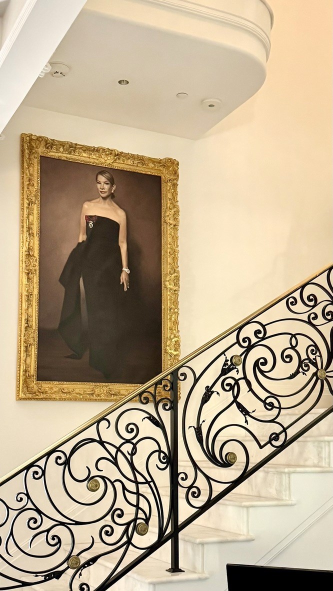 Large gilt-framed formal portrait painting hung above an ornate wrought-iron staircase railing