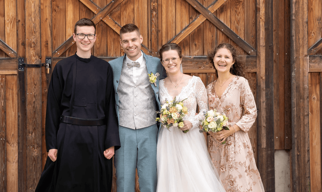 Brautpaar mit Angehörigen vor rustikalem Holztor während Hochzeit in Mallersdorf, Niederbayern