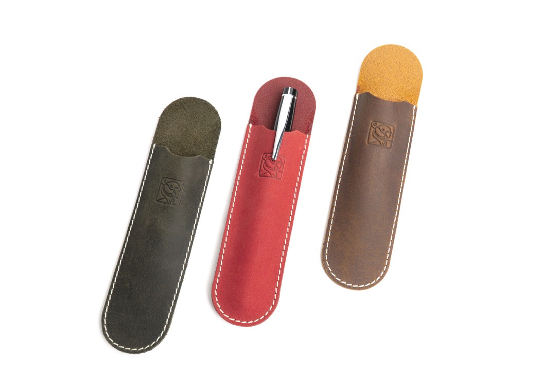 Three pen sleeves in black, red, and brown arranged side-by-side; the center one holds a silver pen.