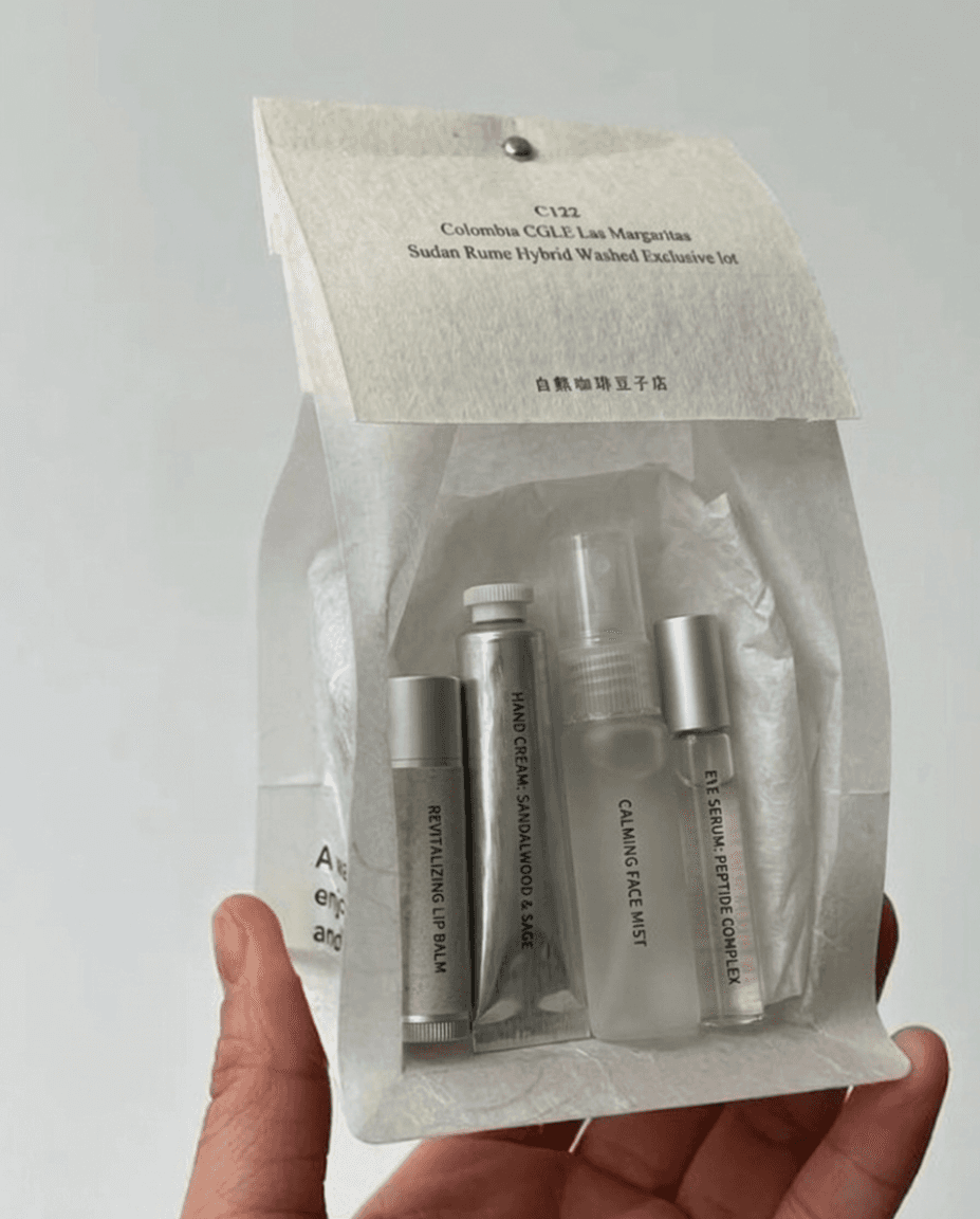 Eco-friendly Paper pouch containing four travel-sized skincare products held up by a hand. Includes lip balm, hand cream, face mist, and eye serum. Soft, minimalistic design.