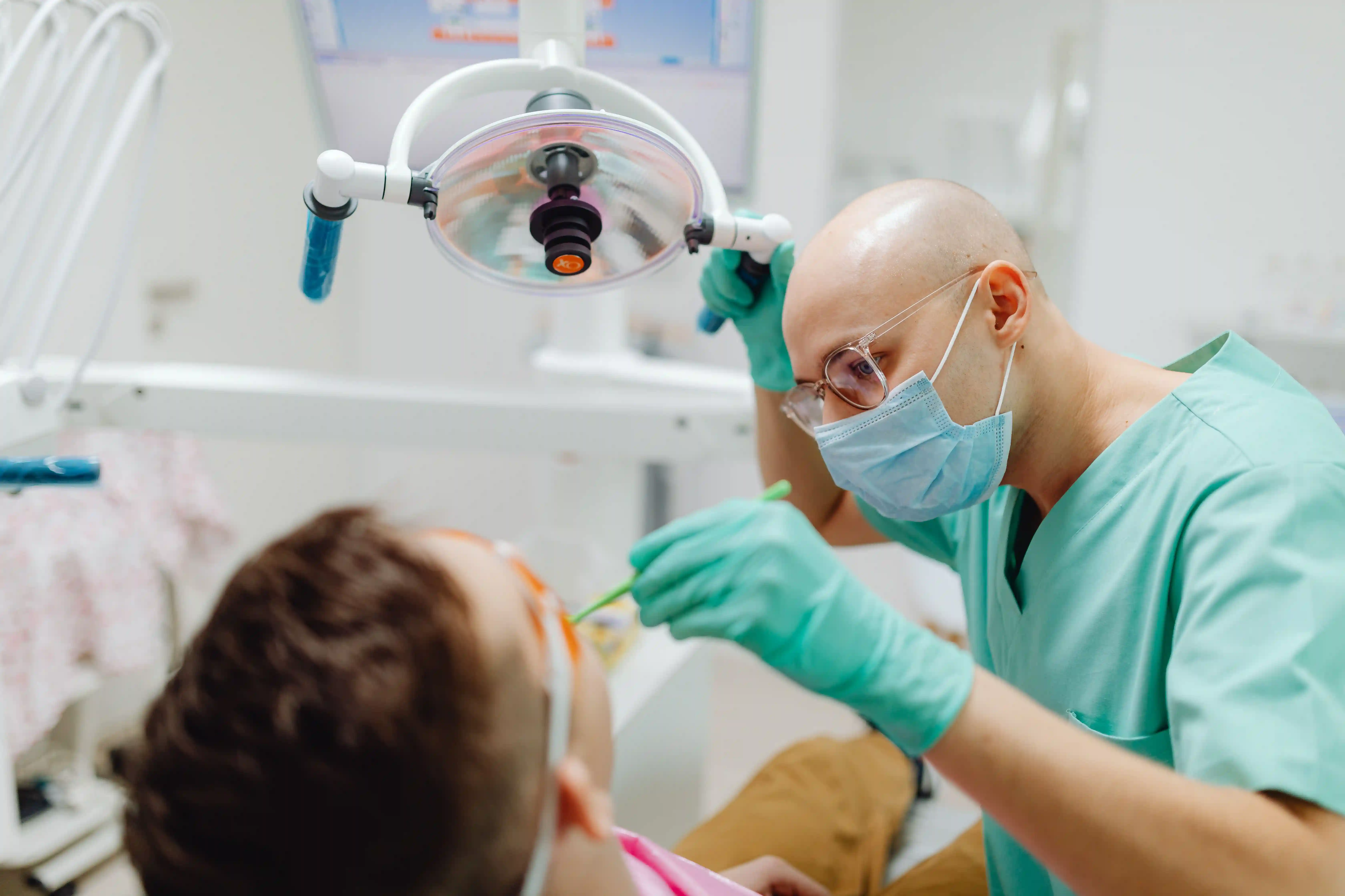 Male dentist in green surgical scrubs smiling in modern dental office.