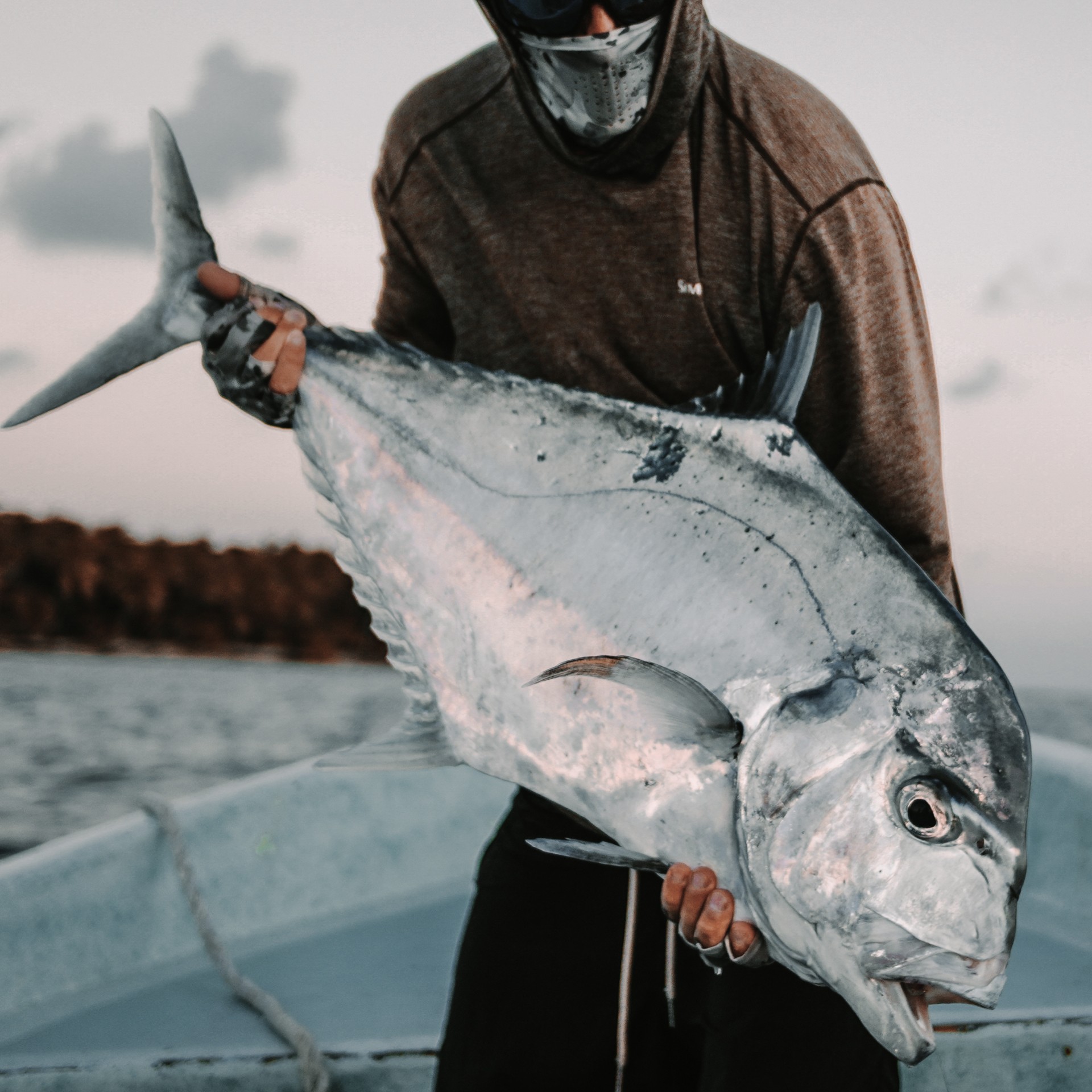 Person standing inside a boat holding a big african pompano in dusk lighting