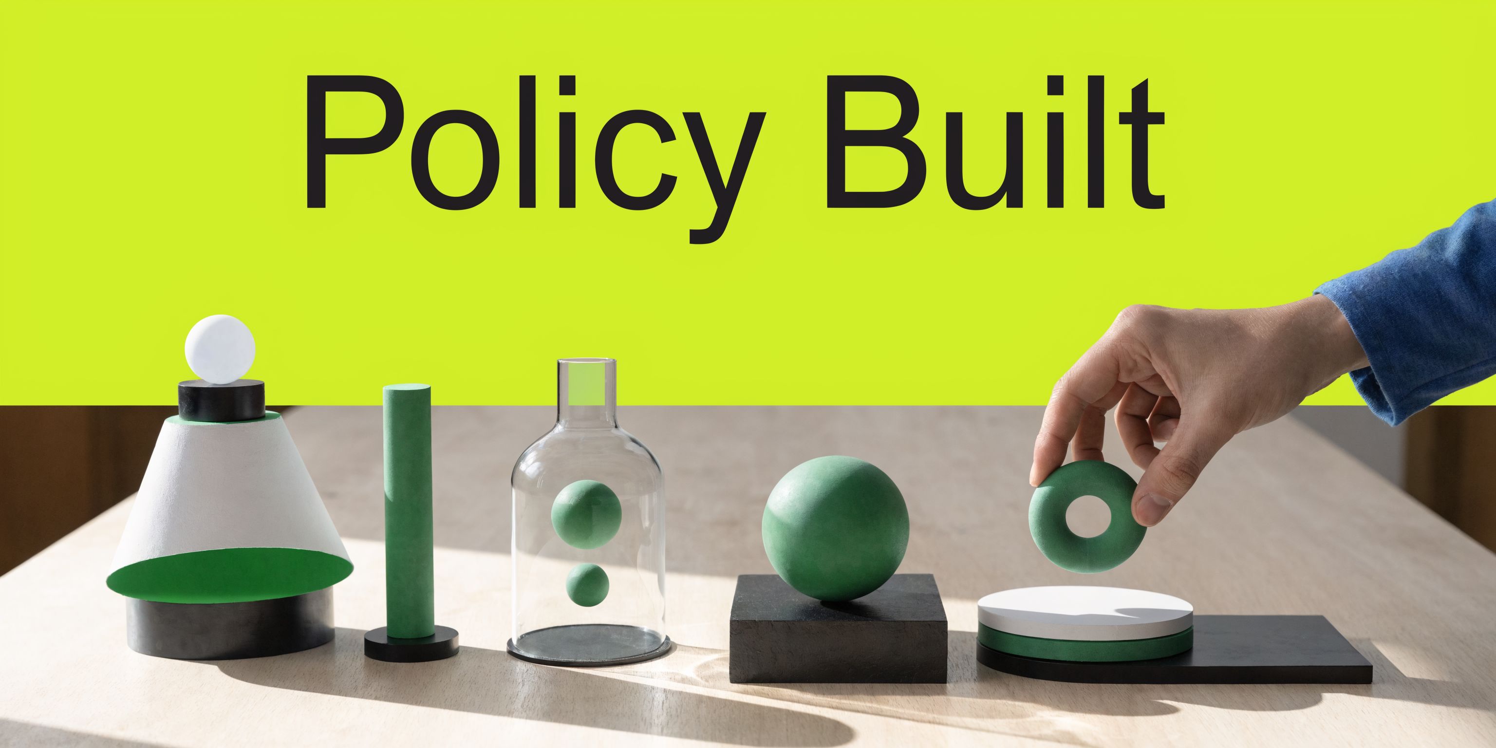 A hand placing a green ring on a block sculpture representing building a policy or strategy.