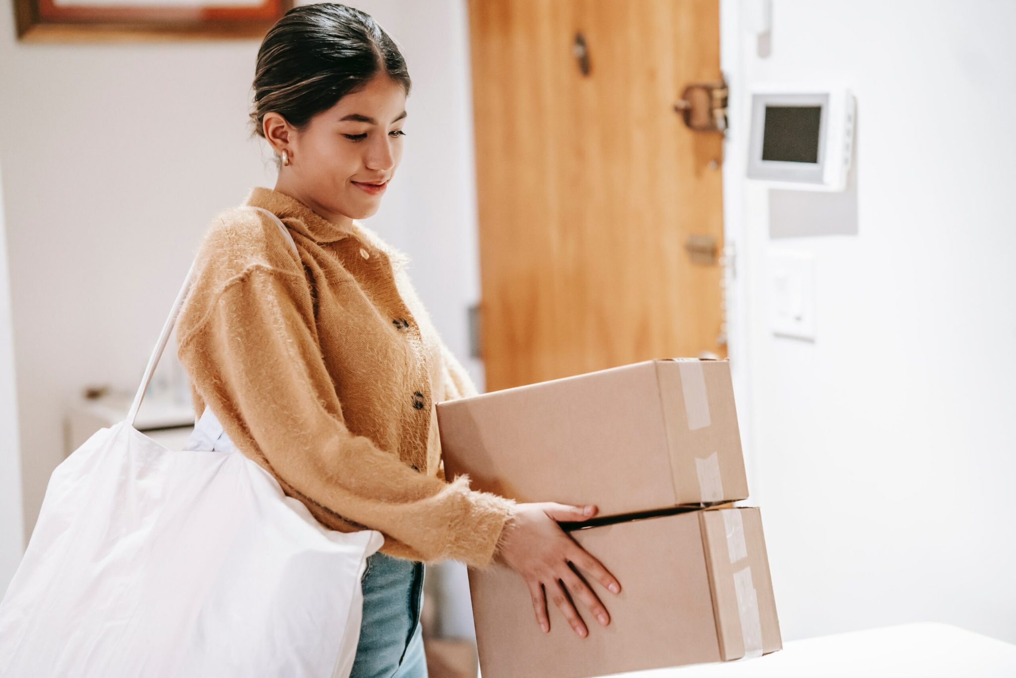 Woman carrying cardboard boxes and a large white bag indoors