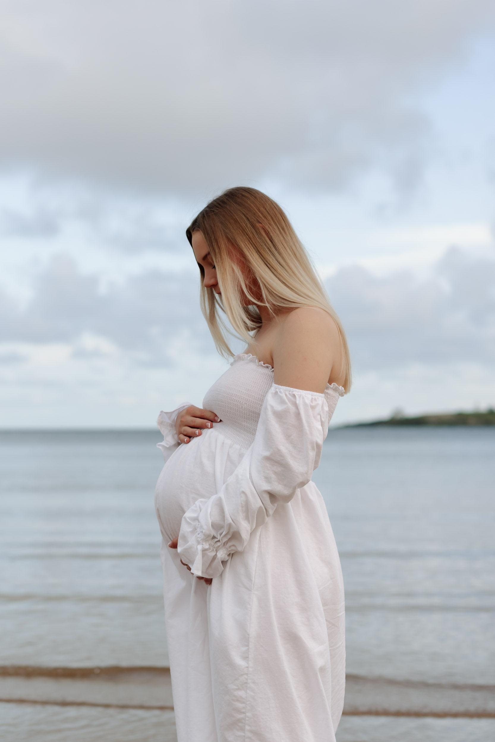 Expecting mother holding her baby bump near the ocean in Mackay