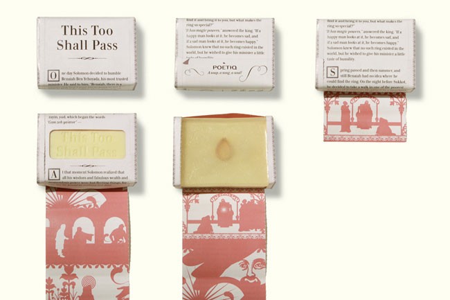 The image shows five small boxes arranged on a white background. Each box contains a single bar of soap with a pale yellow or cream-colored interior and a single darker brown mark on top. The boxes are labeled “This Too Shall Pass” in black text, with some boxes featuring red and white decorative elements on the sides. The labels also include text in a different language, likely describing the soap’s properties or scent. The boxes are arranged in two rows of two, with the top row slightly offset from the bottom. Each box has a white top and bottom section.