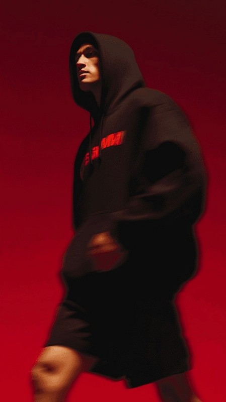 Profile of a man in a black hoodie against a solid red background.